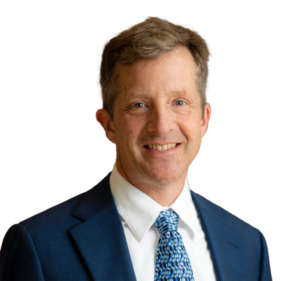 A white man with short light brown hair wearing a dark blue suit jacket, white shirt, and a light blue tie.