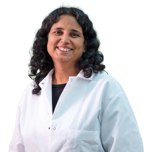 Indian woman with medium length dark curly hair wearing a white lab coat.