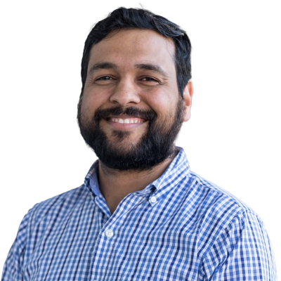 Indian man with black hair and facial hair wearing a blue plaid button down shirt.