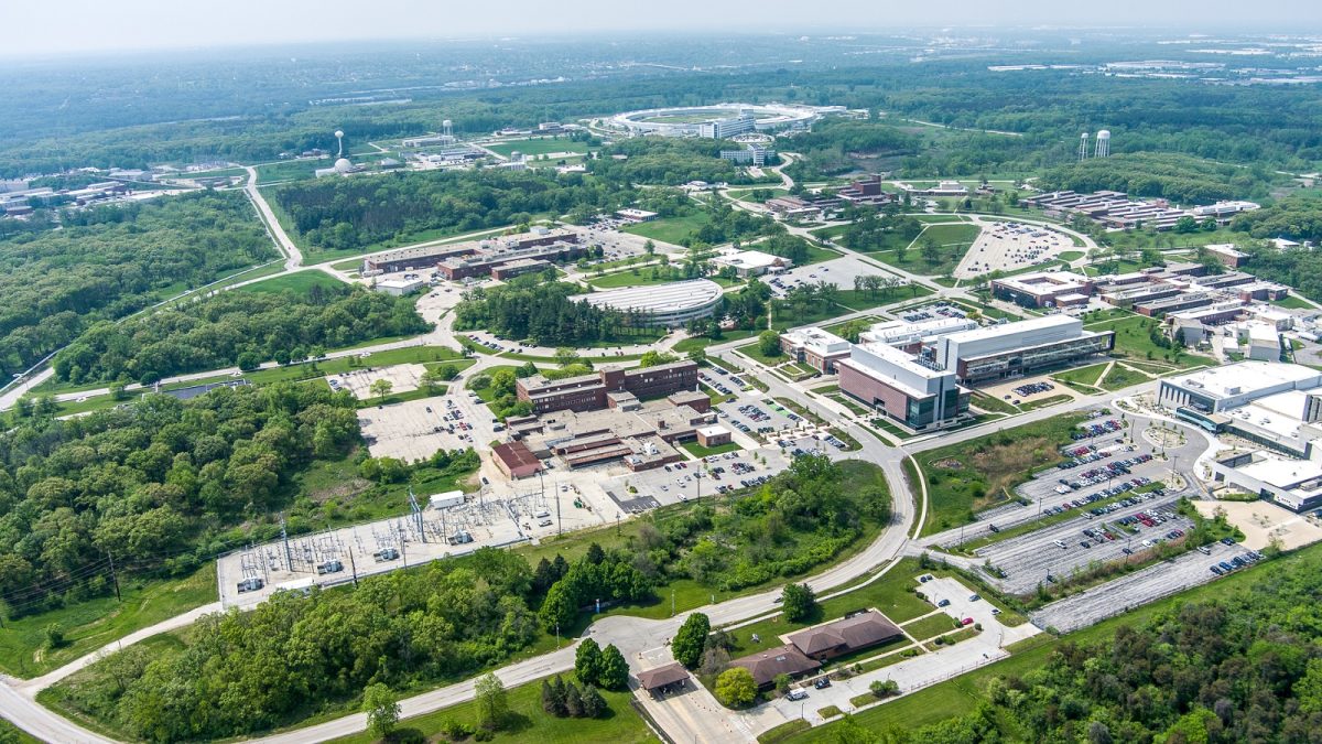 aerial view of a cluster of buildings and parking lots, nestled amongst green trees