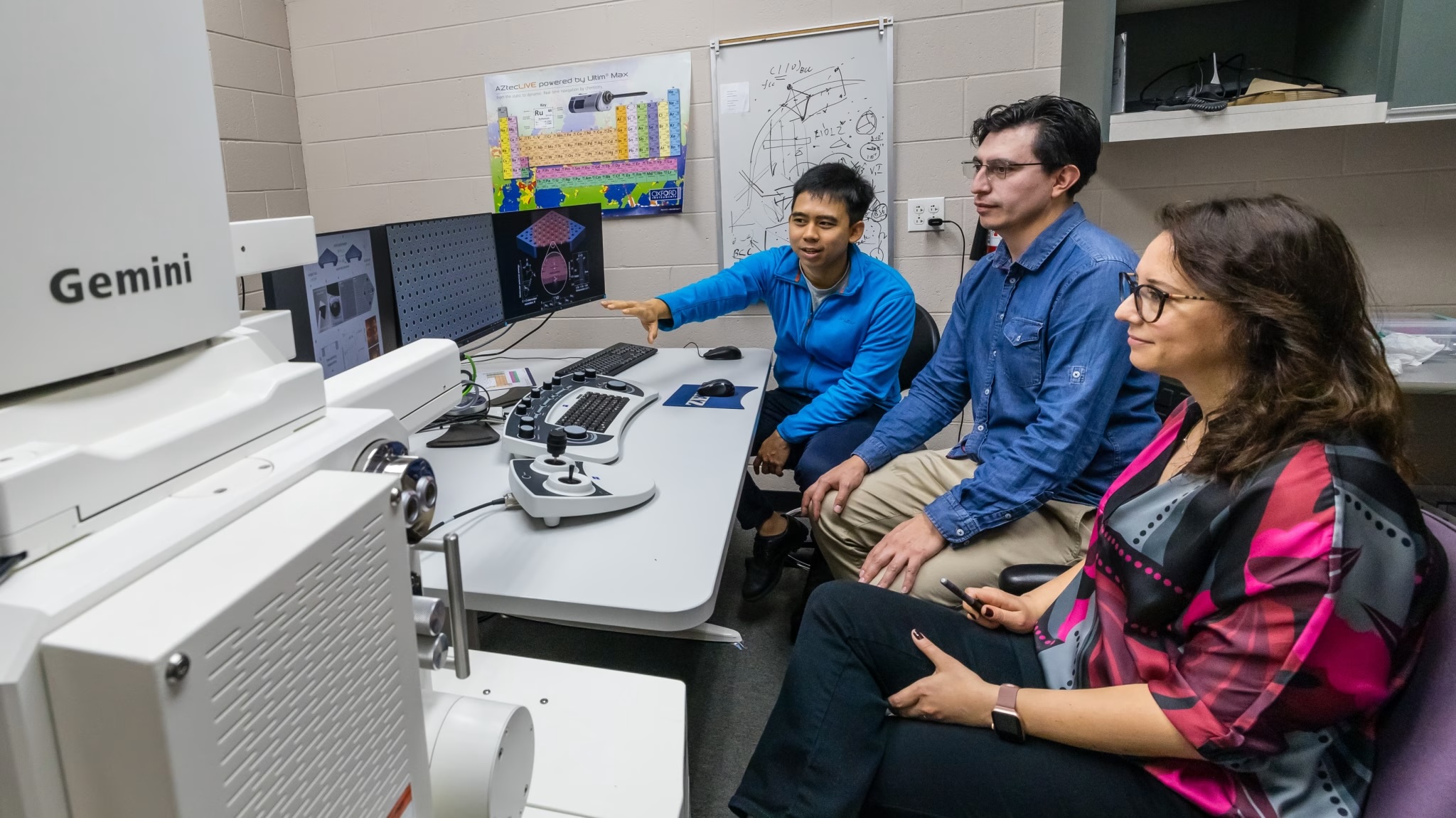 Three people sit around a computer, one gestures toward the screen.