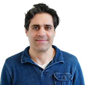 White man with black hair wearing a dark blue jean colored button down shirt.