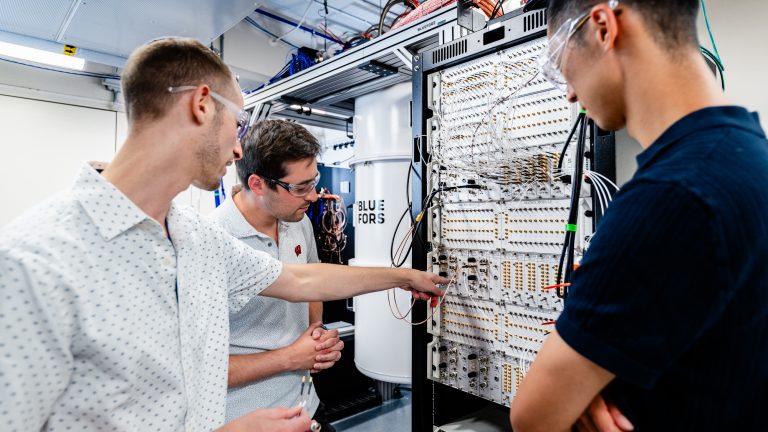 three men wear safety glasses and observe an electronic board