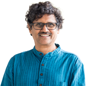 Middle eastern man with curly dark hair wearing glasses and a blue button down shirt.