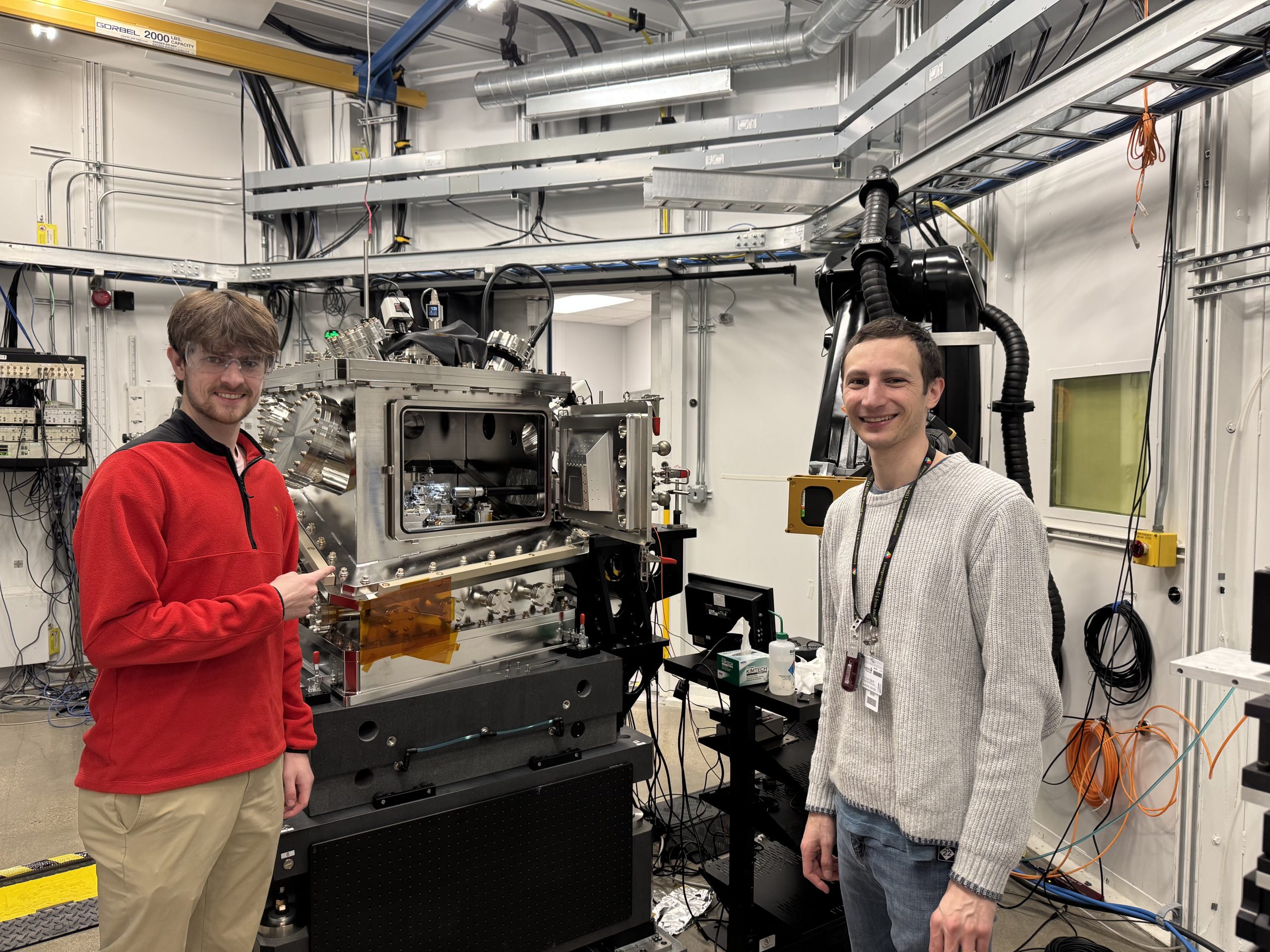 two men standing in a lab room with silver technical equipment.
