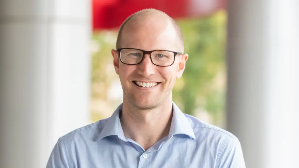 Photo of a friendly bald white man wearing glasses and a light blue button down shirt.