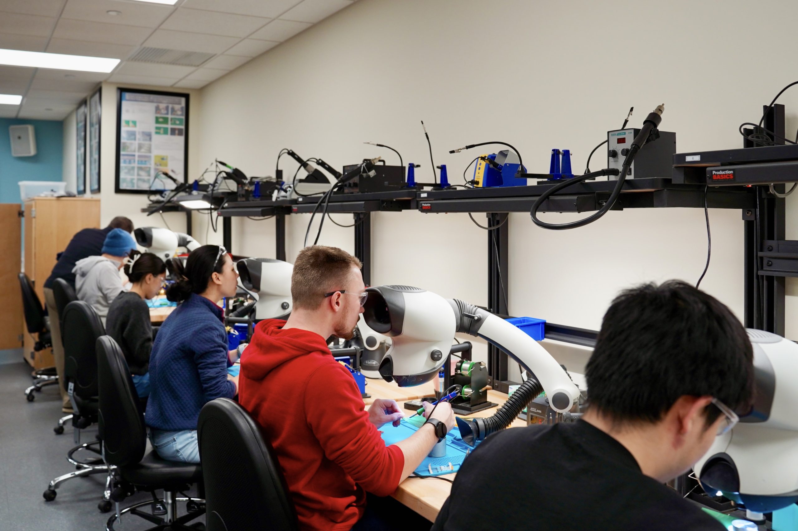Engineering students sit at individual soldering stations in a classroom